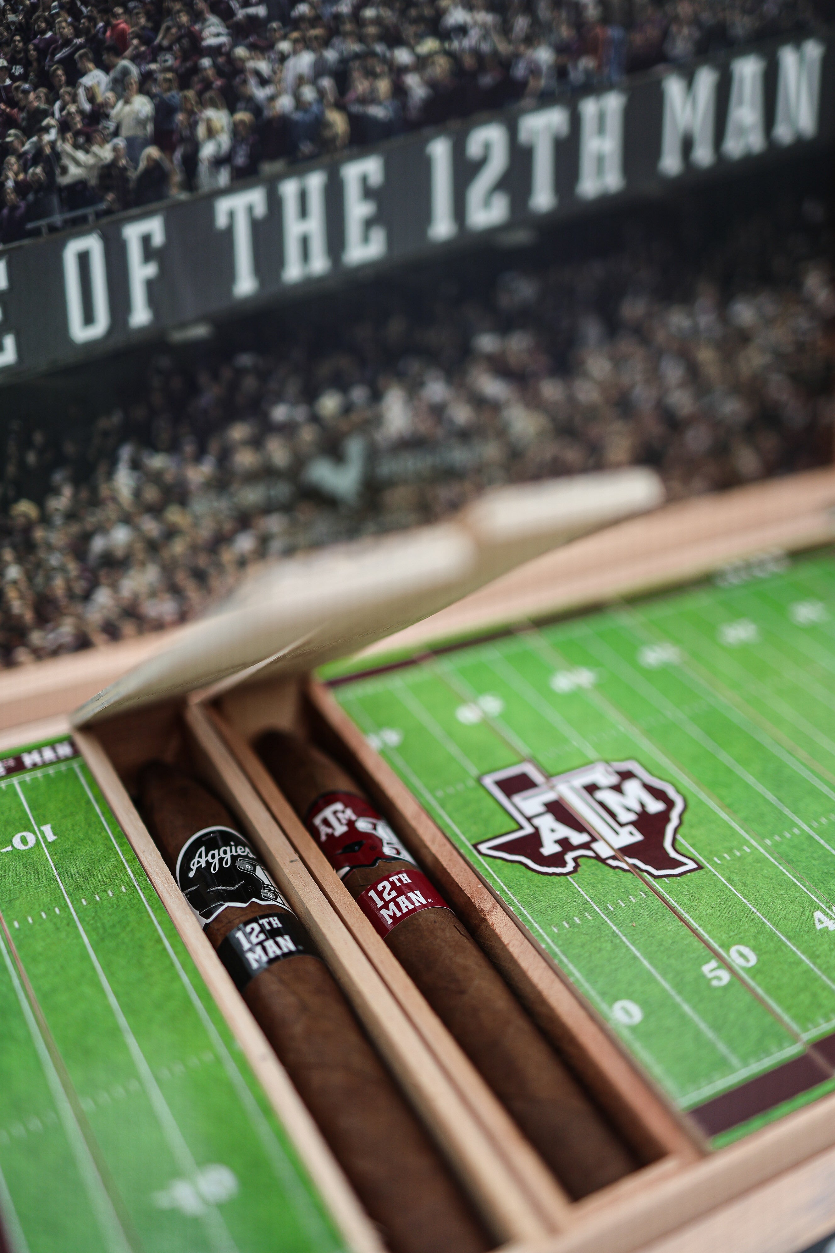 Cigar box with cigars featuring a football field design and '12th Man' logo, with a stadium background.